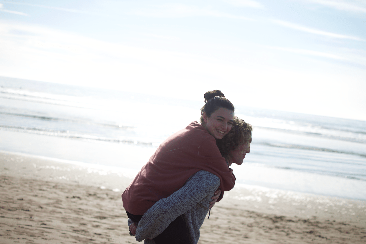 Two people at the beach, one giving the other a piggyback ride