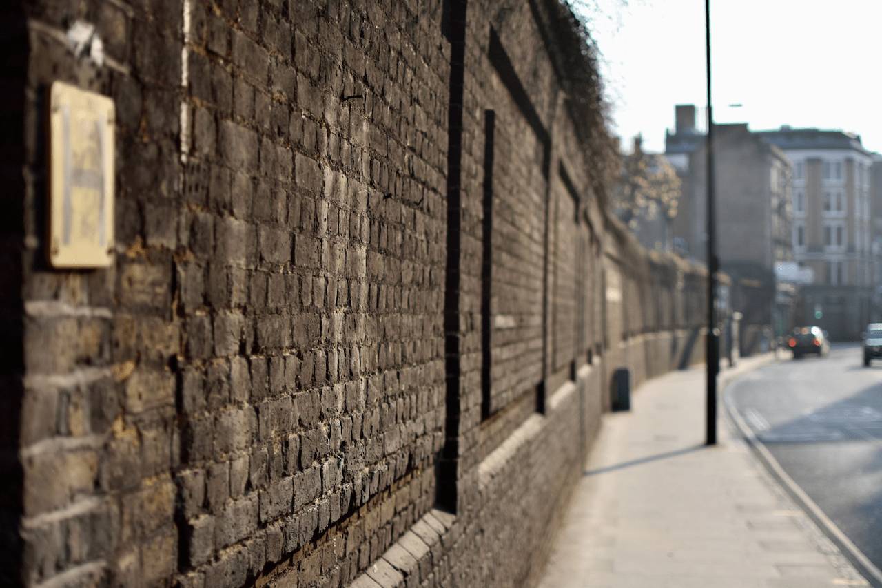 Weathered brick wall along a city street with a small framed item mounted on it