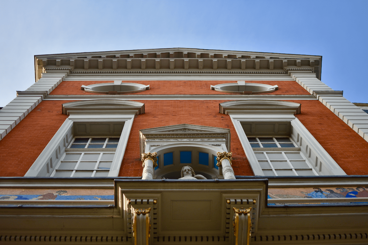 Upward view of a classical red brick building with ornate white trim and a sculptural bust