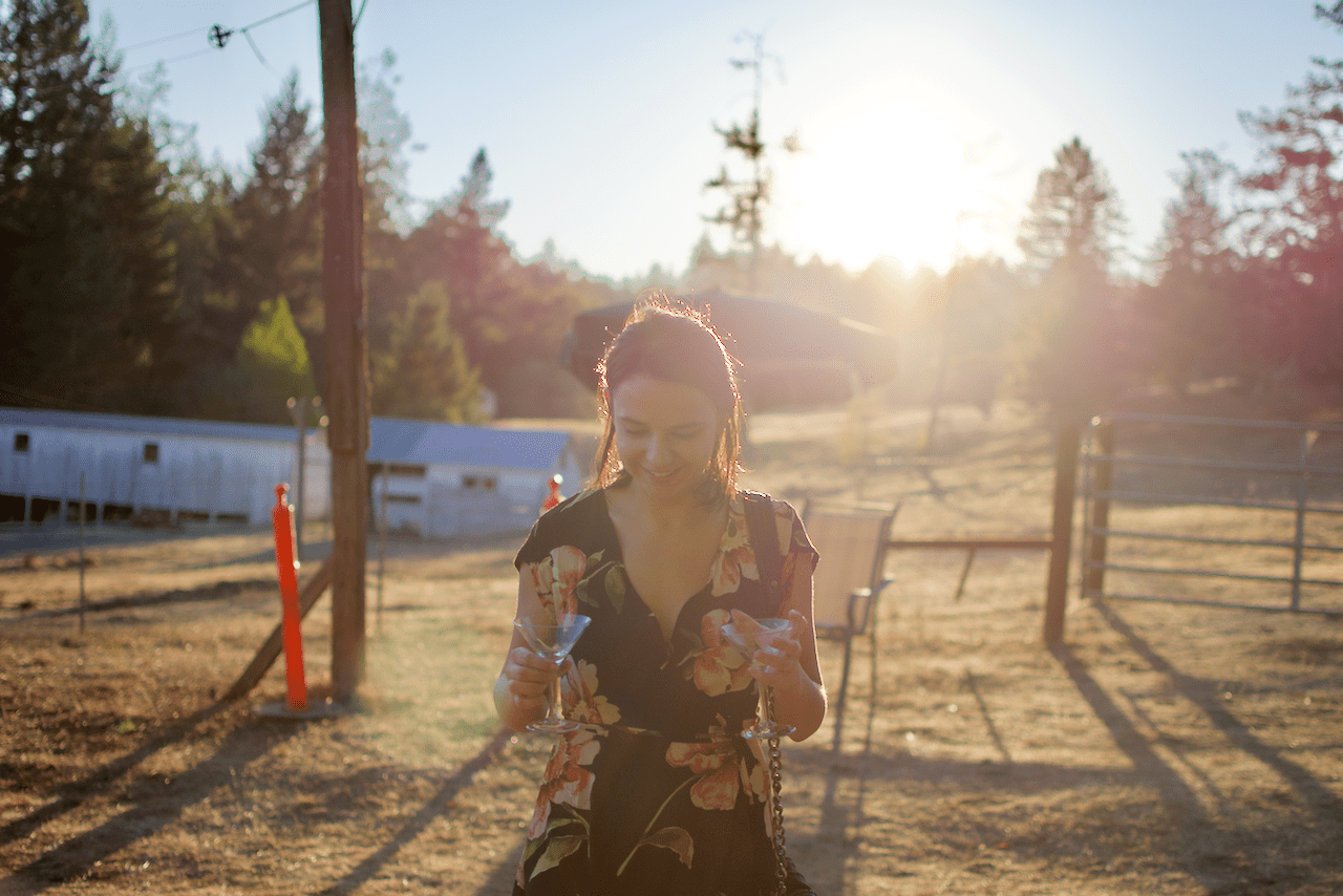 Person in a floral dress holding glasses during golden hour with sunset in the background